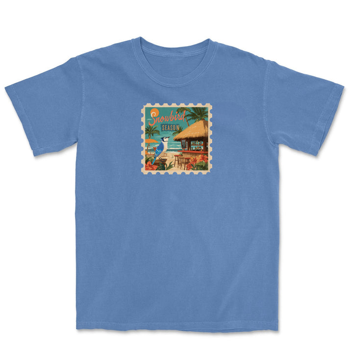 Blue t-shirt with a tropical stamp design featuring a hut and palm trees on a white background.