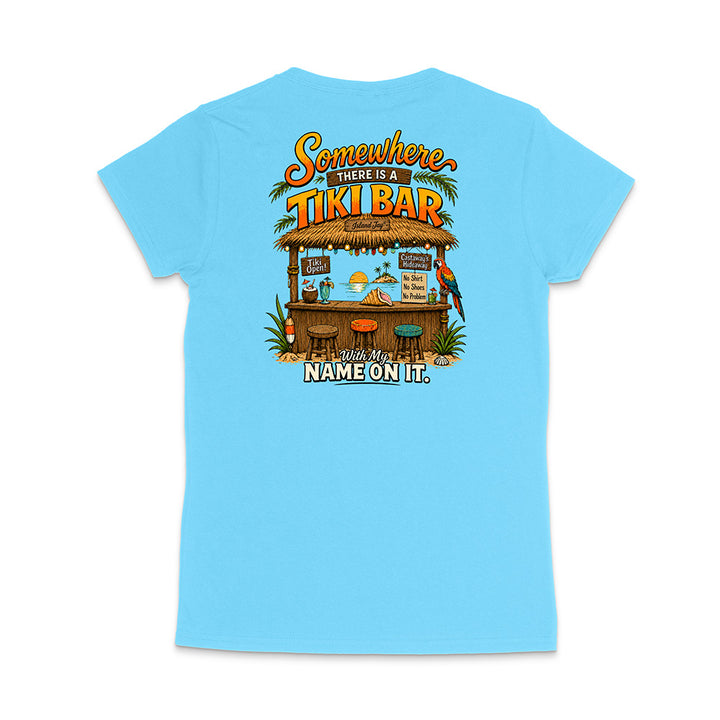 A light blue short-sleeve t-shirt shown from the back, featuring a colorful graphic of a tropical 'Tiki Bar' with the text 'Somewhere there is a TIKI BAR' and 'With my NAME ON IT.'.