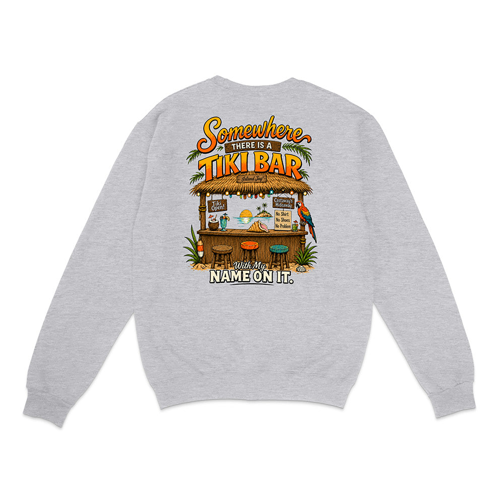 A light heather gray crewneck sweatshirt shown from the back, featuring a colorful graphic print of a tropical tiki bar with parrots and the text 'Somewhere there is a TIKI BAR with my NAME ON IT.'.