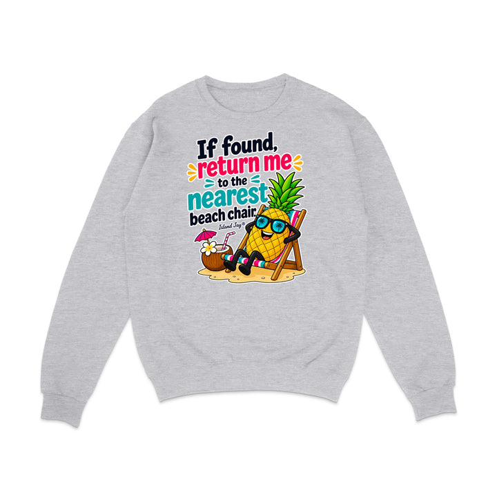 A light heather gray crewneck sweatshirt featuring a colorful graphic print of a pineapple character wearing sunglasses and reclining in a beach chair next to a coconut drink, with the text 'If found, return me to the nearest beach chair' in black, pink, and teal lettering.