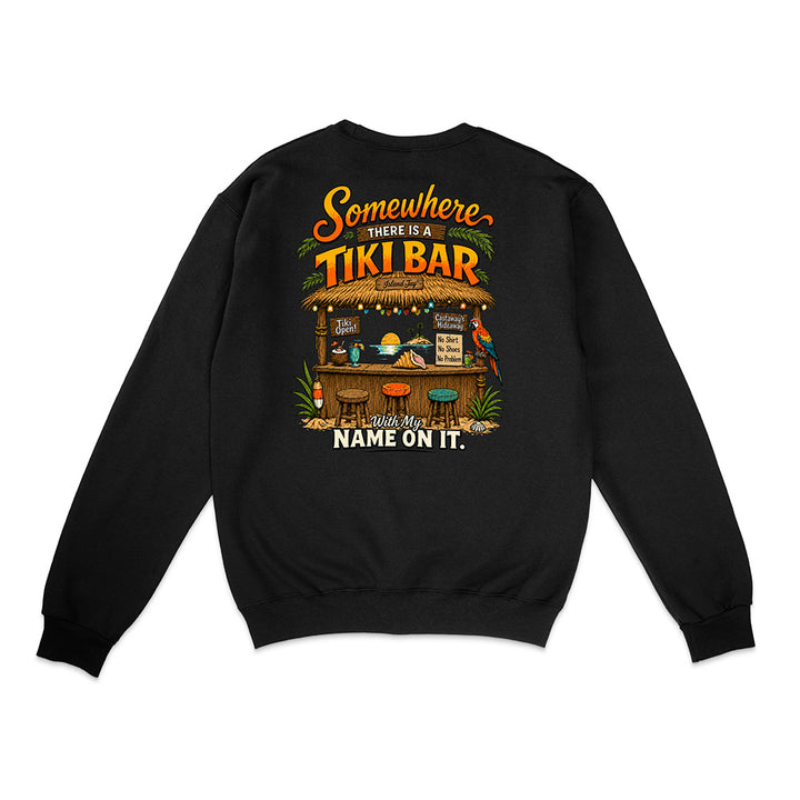 A black crewneck sweatshirt shown from the back, featuring a colorful graphic print of a tropical tiki bar with the text 'Somewhere THERE IS A TIKI BAR and my NAME ON IT.'.