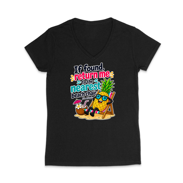 A black women's V-neck t-shirt with a colorful graphic print on the front. The graphic features a pineapple character wearing sunglasses and sitting in a beach chair next to a coconut drink, with the text 'If found, return me to the nearest beach chair' in a retro font.