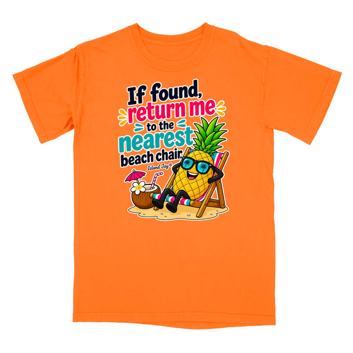 An orange short-sleeve crewneck t-shirt featuring a colorful cartoon graphic of a pineapple wearing sunglasses and sitting in a beach chair on a sandy beach, with the text 'If found, return me to the nearest beach chair' and 'Made by'.