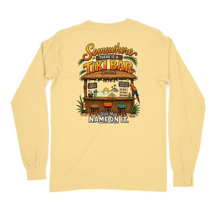 A pale yellow long-sleeve t-shirt shown from the back, featuring a colorful graphic print of a tropical 'Tiki Bar' with the text 'Somewhere There Is A Tiki Bar. And My Name On It.