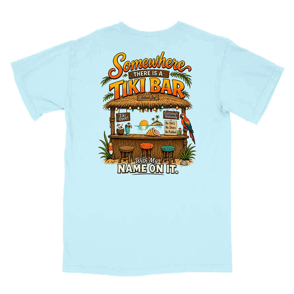 A light blue short-sleeve t-shirt shown from the back, featuring a colorful graphic of a tropical tiki bar with the text 'Somewhere THERE IS A TIKI BAR' and 'With My NAME ON IT.'.