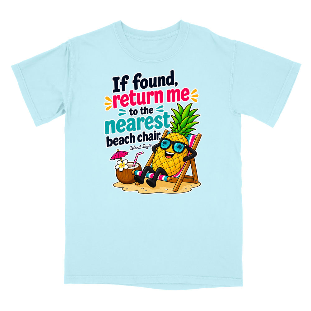 A light blue short-sleeve t-shirt with a colorful graphic of a pineapple character wearing sunglasses and reclining on a beach chair next to a coconut drink, with the text 'If found, return me to the nearest beach chair' and 'Island Style!'.