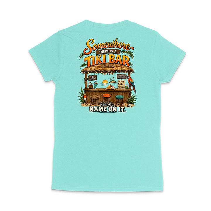 A light aqua blue short-sleeve t-shirt shown from the back, featuring a colorful graphic of a tropical 'Tiki Bar' with the text 'Somewhere there is a TIKI BAR' and 'With my NAME ON IT'.