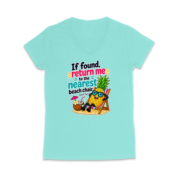 A light aqua V-neck t-shirt with a colorful graphic on the front. The graphic features a pineapple character wearing sunglasses and sitting in a beach chair on a sandy surface, next to a coconut drink, with the text 'If found, return me to the nearest beach chair'.