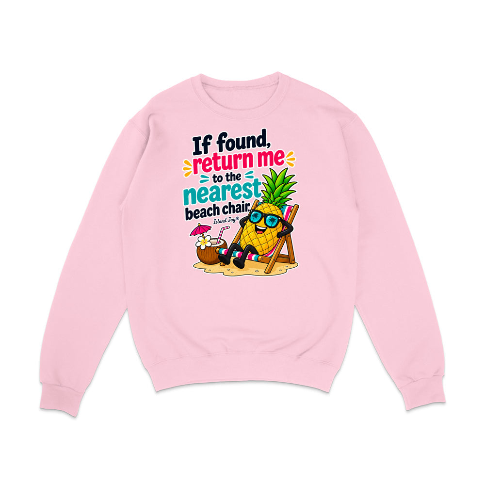 A light pink crewneck sweatshirt featuring a colorful graphic of a pineapple character wearing sunglasses and reclining in a beach chair on a sand dune, next to a coconut drink with a pink umbrella. Above the graphic is the text 'If found, return me to the nearest beach chair' in black, blue, and pink lettering.