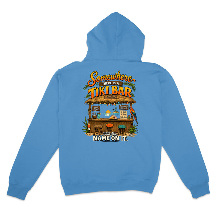 A light blue hoodie shown from the back, featuring a colorful graphic print of a tropical 'Tiki Bar' with the text 'Somewhere THERE IS A TIKI BAR' and 'NAME ON IT.'.