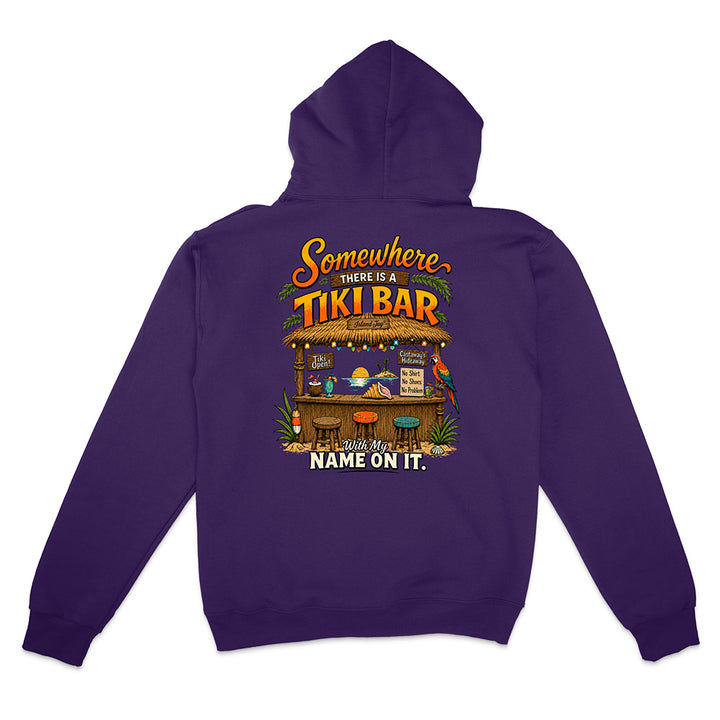A purple pullover hoodie shown from the back, featuring a colorful graphic print of a tiki bar with the text 'Somewhere THERE IS A TIKI BAR' and 'NAME ON IT.'.