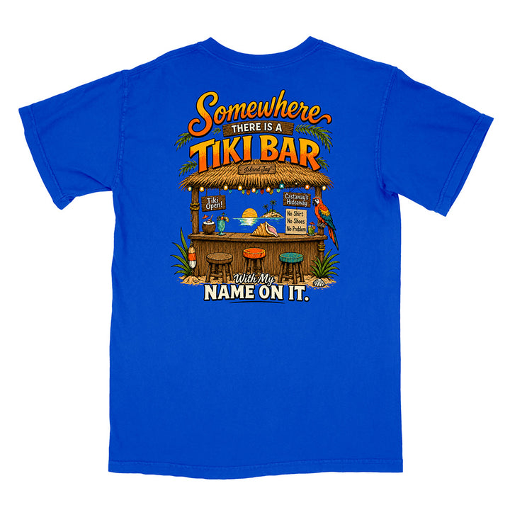 A royal blue short-sleeve t-shirt with a large graphic print on the back featuring a tropical tiki bar scene and the text 'Somewhere THERE IS A TIKI BAR with my NAME ON IT.'.