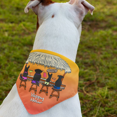 A beach dog wearing a funny Island Jay Dog Bandana that says Yappy Hour on it. It shows dogs siting at a beach bar.
