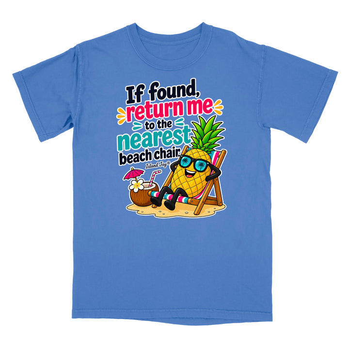 A blue short-sleeve crewneck t-shirt featuring a colorful graphic of a pineapple wearing sunglasses and relaxing in a beach chair next to a coconut drink, with the text 'If found, return me to the nearest beach chair' printed on the front.
