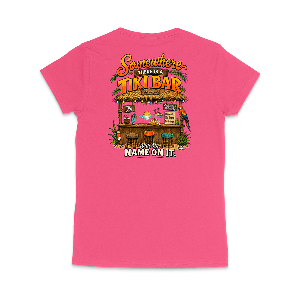 A bright pink women's short-sleeve t-shirt shown from the back, featuring a colorful graphic of a tropical tiki bar with the text 'Somewhere THERE IS A TIKI BAR' and 'With My NAME ON IT.'.