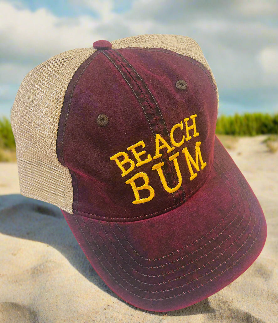 Maroon and beige cap with 'Beach Bum' text on a sandy background