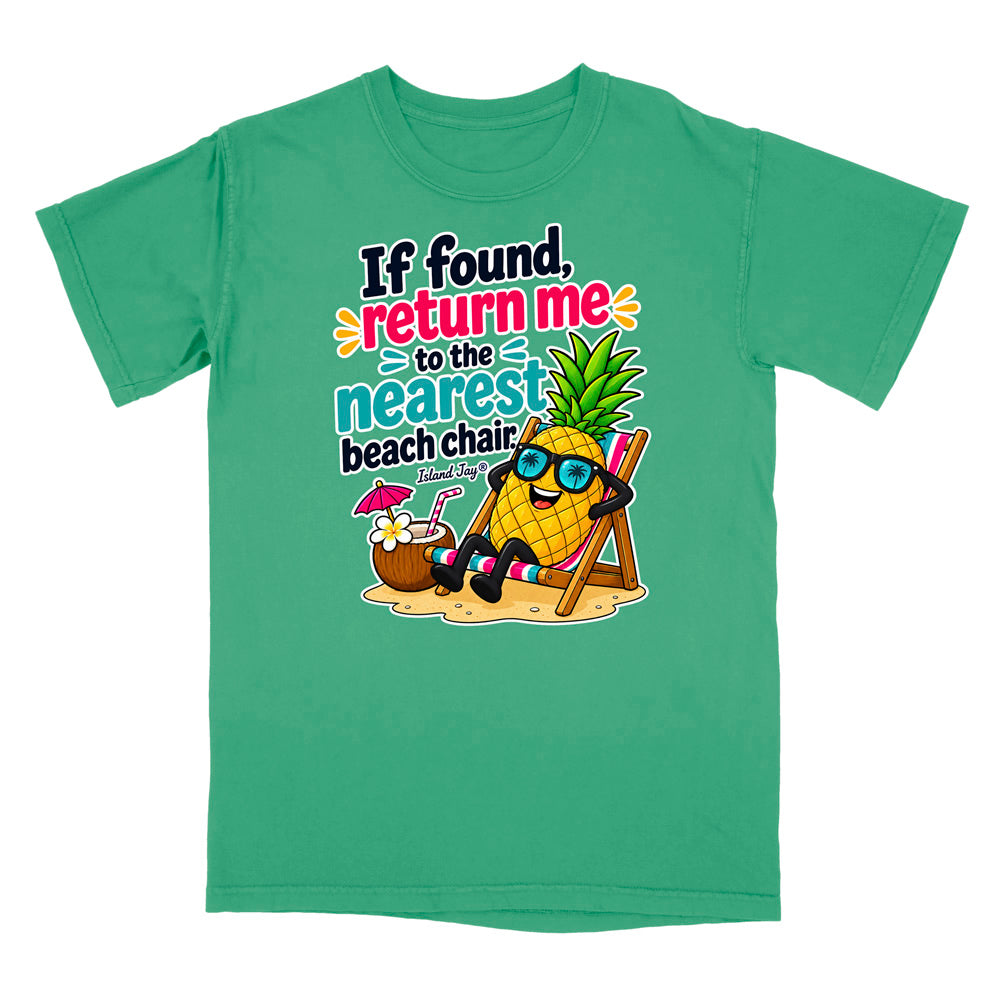 A green short-sleeve crewneck t-shirt featuring a colorful graphic of a pineapple wearing sunglasses and relaxing in a beach chair next to a coconut drink, with the text 'If found, return me to the nearest beach chair' printed on the front.