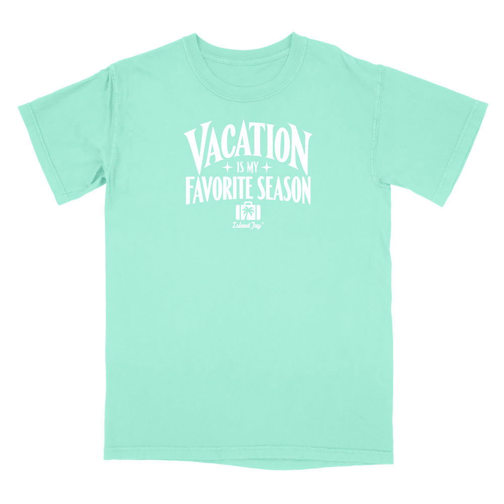 A mint green short-sleeve t-shirt with a white graphic print on the front that reads 'VACATION IS MY FAVORITE SEASON' with a small 'Travel Dog' logo underneath, displayed on a solid white background.