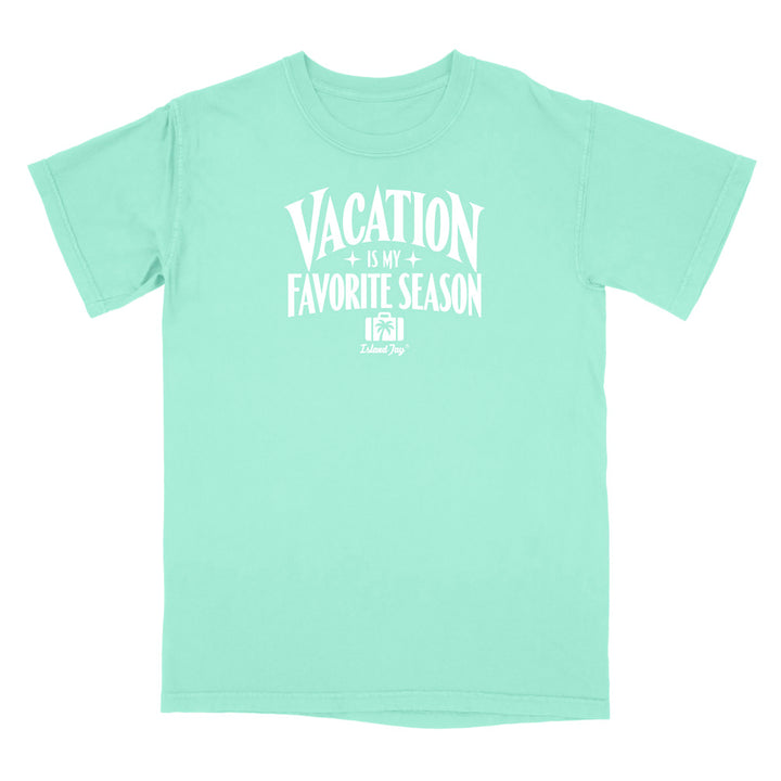 A mint green short-sleeve t-shirt with a white graphic print on the front that reads 'VACATION IS MY FAVORITE SEASON' with a small 'Travel Dog' logo underneath, displayed on a solid white background.