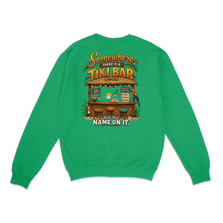 A bright green crewneck sweatshirt shown from the back, featuring a colorful graphic of a tropical 'Tiki Bar' with the text 'Somewhere THERE IS A TIKI BAR and my NAME ON IT.'.