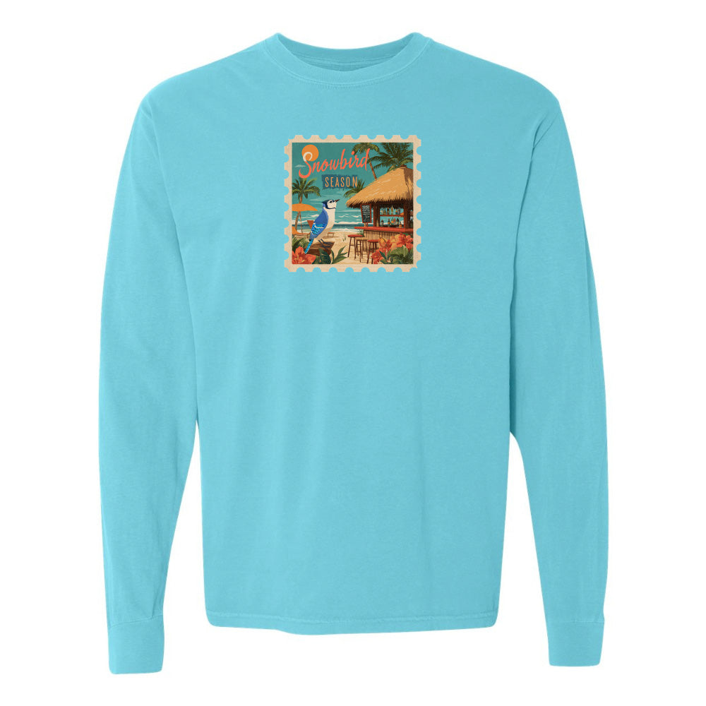 Light blue long-sleeve shirt with a graphic of a beach scene and palm trees on a white background.