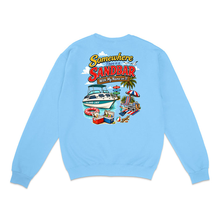 A light blue crewneck sweatshirt shown from the back, featuring a colorful graphic print with the text 'Somewhere I've Been ISLAND' and an illustration of a boat, beach umbrella, palm tree, and poolside scene.