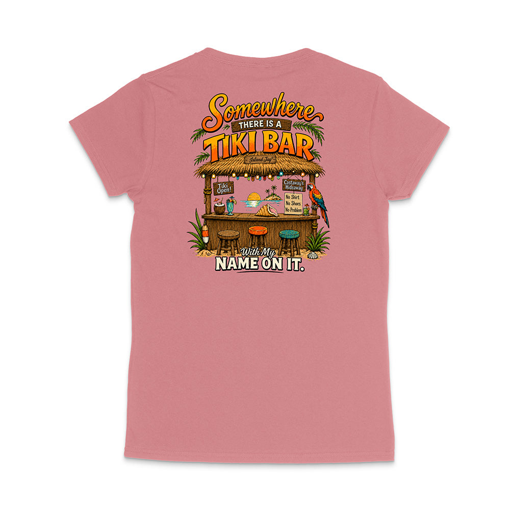 A pink short-sleeve t-shirt shown from the back, featuring a colorful graphic of a tropical 'Tiki Bar' with the text 'Somewhere there is a TIKI BAR' and 'With my NAME ON IT.'.