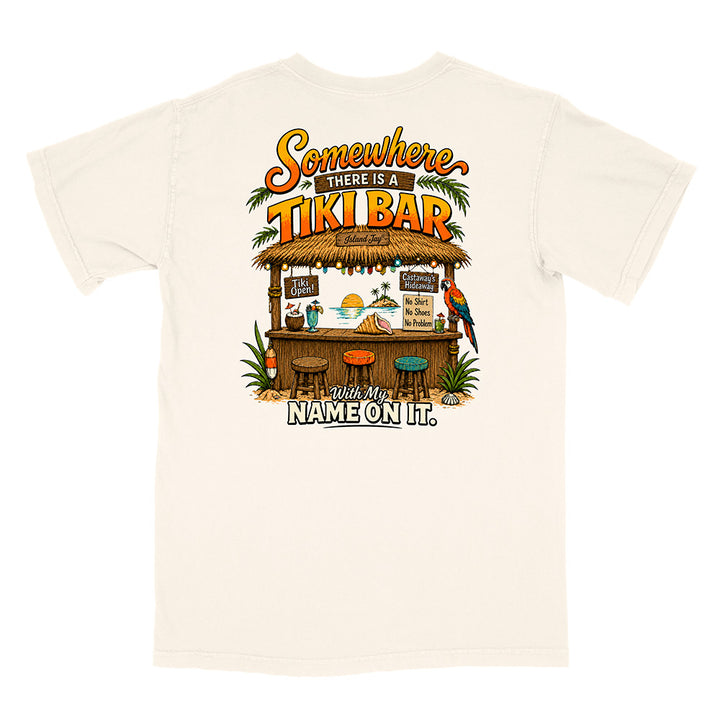 An off-white short-sleeve t-shirt with a colorful graphic print on the front depicting a tropical tiki bar, parrots, and the text 'Somewhere THERE IS A TIKI BAR With My NAME ON IT.'.