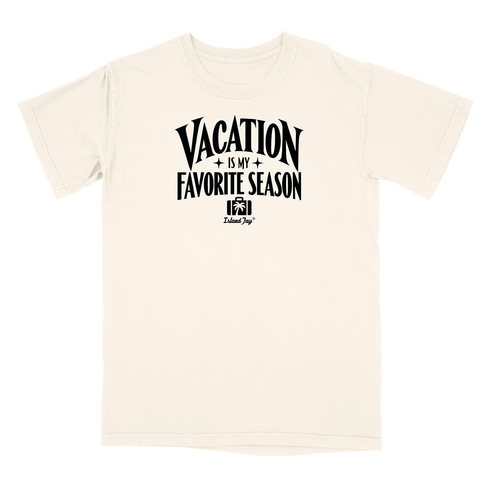 An off-white short-sleeve t-shirt with a black graphic print on the chest that reads 'VACATION IS MY FAVORITE SEASON' with a small camera icon and 'Travel Dog' branding underneath, displayed on a solid white background.