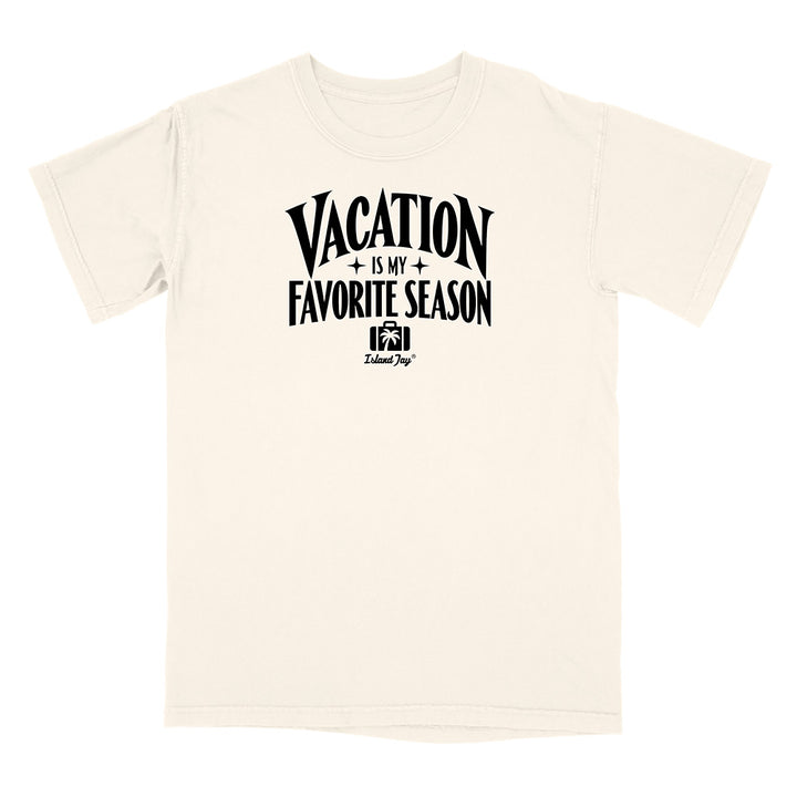 An off-white short-sleeve t-shirt with a black graphic print on the chest that reads 'VACATION IS MY FAVORITE SEASON' with a small camera icon and 'Travel Dog' branding underneath, displayed on a solid white background.