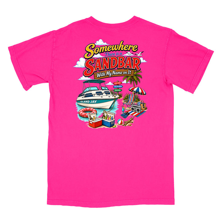 A bright pink short-sleeve t-shirt with a colorful graphic print on the front. The graphic features the text 'Somewhere I'll Be at the Sandbar With My Name on It' in a retro yellow and red font, above an illustration of a white motorboat, a beach umbrella, a cooler, and a beach ball.