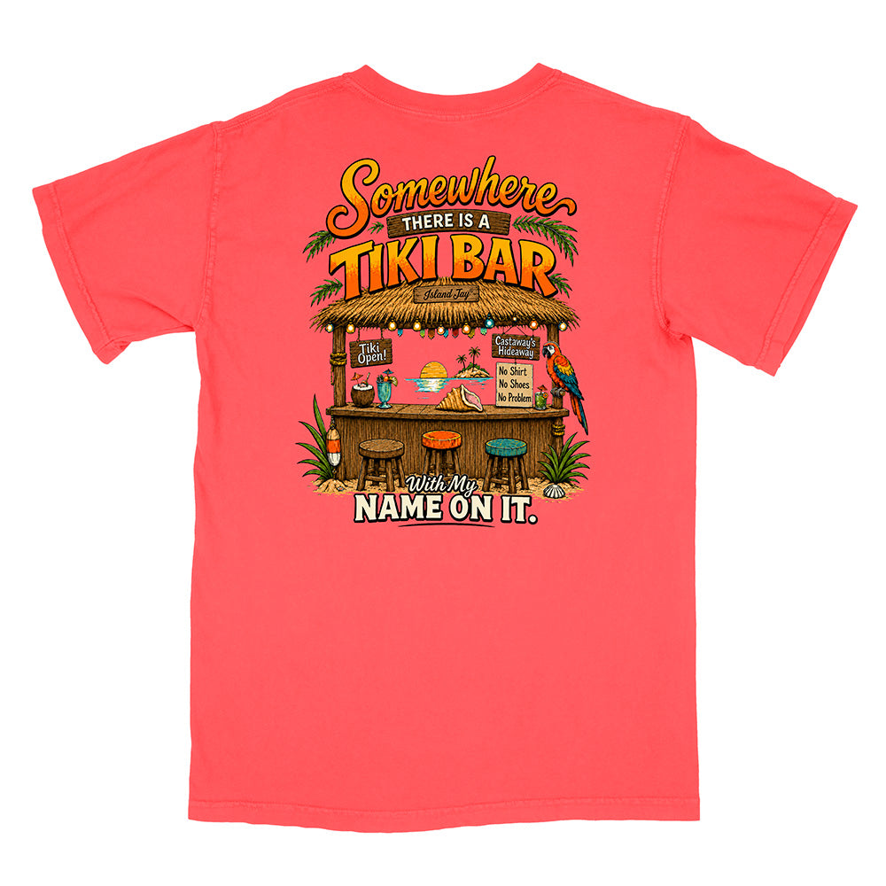 A coral pink short-sleeve t-shirt shown from the back, featuring a colorful graphic of a tropical tiki bar with the text 'Somewhere THERE IS A TIKI BAR' and 'Make My NAME ON IT.'.