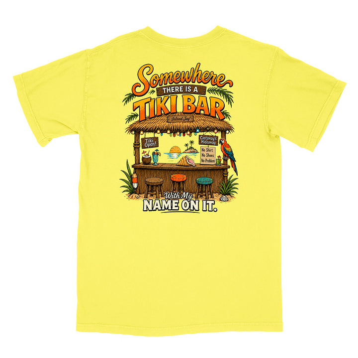 A bright yellow short-sleeve t-shirt shown flat against a white background, featuring a colorful graphic print on the back with a tiki bar illustration and the text 'Somewhere there is a TIKI BAR' and 'I'll have my NAME ON IT.'.