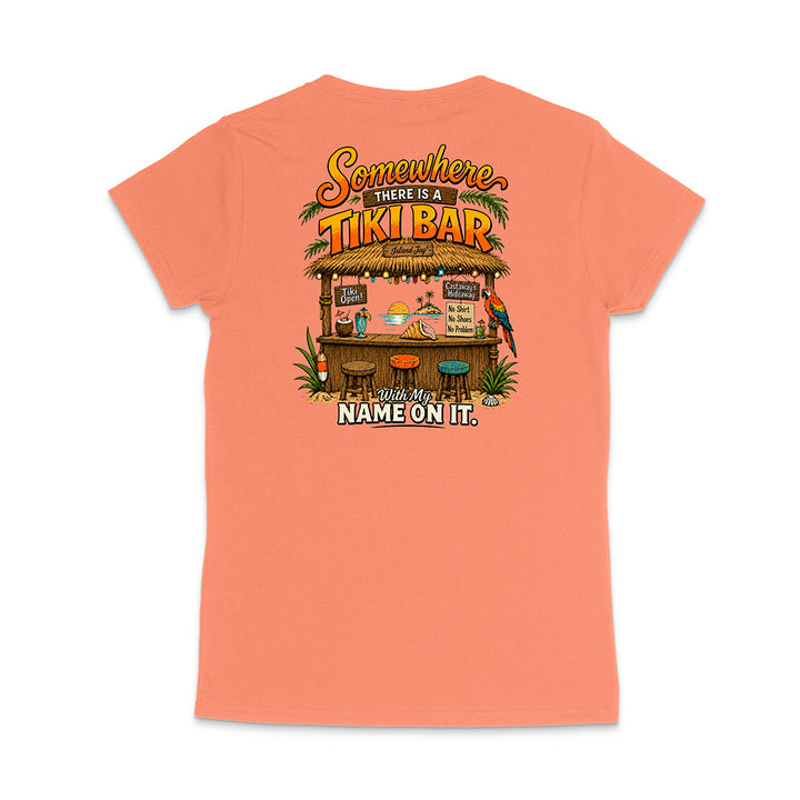 A coral pink short-sleeve t-shirt shown from the back, featuring a colorful graphic of a tropical 'Tiki Bar' with the text 'Somewhere there is a Tiki Bar' and 'With My NAME ON IT.'.