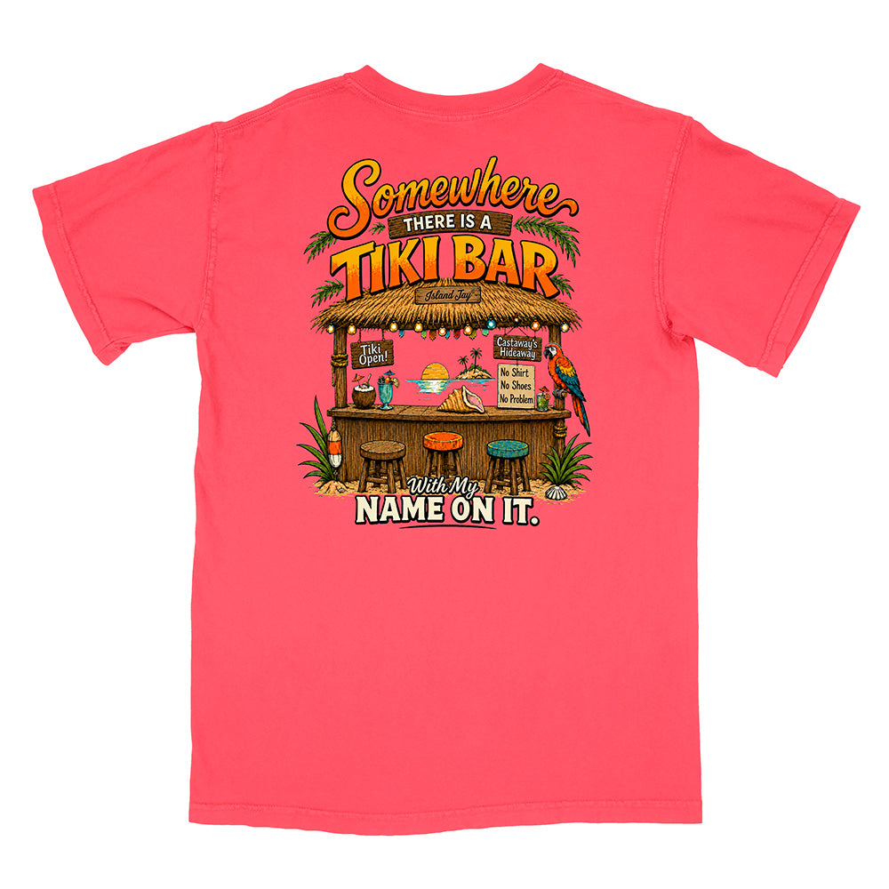 A coral pink short-sleeve t-shirt with a colorful graphic on the back featuring a tropical tiki bar scene and the text 'Somewhere THERE IS A TIKI BAR with My NAME ON IT.'.