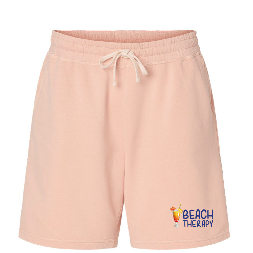 Pink shorts with 'Beach Therapy' text and graphic on a white background
