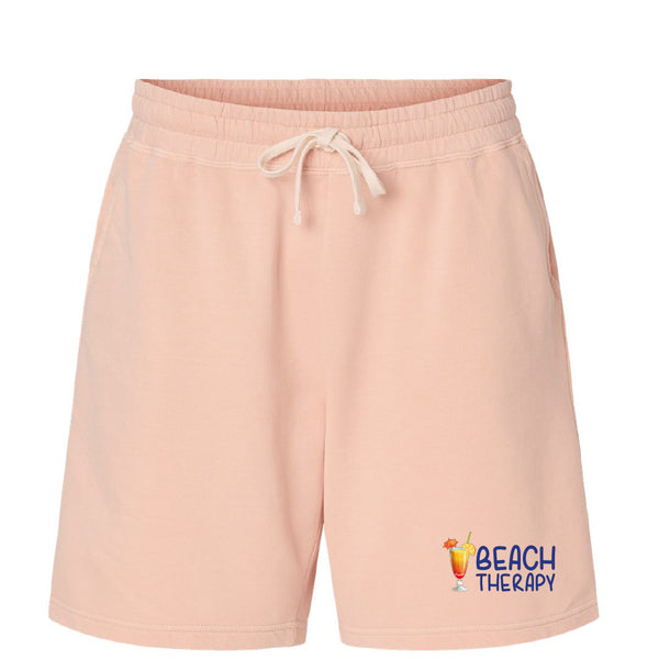 Pink shorts with 'Beach Therapy' text and graphic on a white background