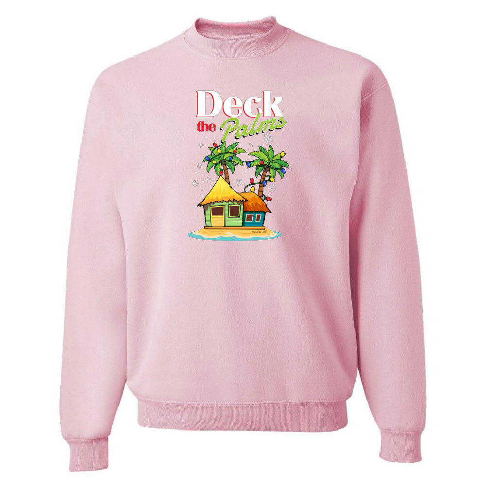 Pink sweatshirt with a tropical hut and palm tree design and graphic text reading "Deck The Palms" on a white background