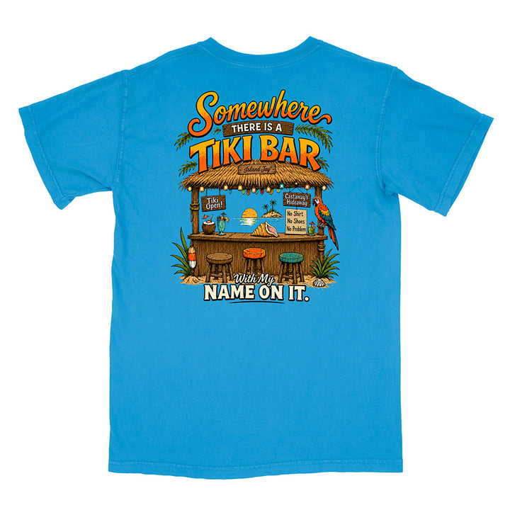 A bright blue short-sleeve t-shirt with a large, colorful graphic on the back. The graphic features a tropical tiki bar scene with a parrot, drinks, and the text 'Somewhere THERE IS A TIKI BAR With My NAME ON IT.