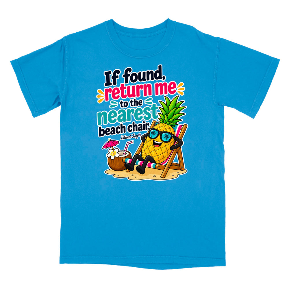 A bright blue short-sleeve t-shirt with a colorful graphic on the front. The graphic features a cartoon pineapple wearing sunglasses and sitting in a beach chair next to a coconut drink, with the text 'If found, return me to the nearest beach chair' in playful multicolor lettering.