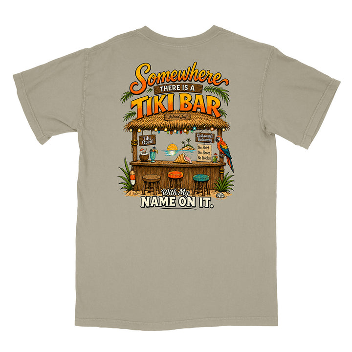 A light gray short-sleeve t-shirt with a colorful graphic print on the back featuring a tiki bar scene and the text 'Somewhere THERE IS A TIKI BAR with My NAME ON IT.'.