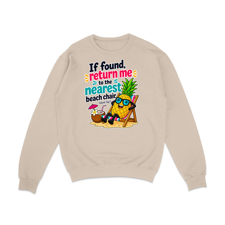 A beige crewneck sweatshirt with a colorful graphic of a pineapple character wearing sunglasses and reclining in a beach chair next to a coconut drink, with the text 'If found, return me to the nearest beach chair' printed on the front.