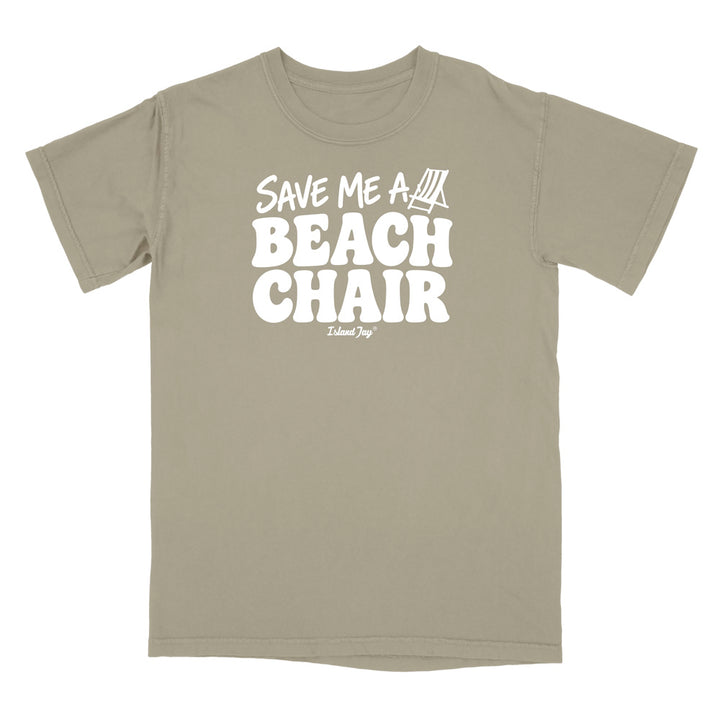 A short-sleeve crewneck t-shirt in a muted khaki-beige color, featuring a bold white graphic print on the front that reads 'SAVE ME A BEACH CHAIR' 
