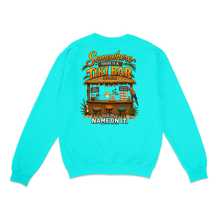 A bright turquoise crewneck sweatshirt shown from the back, featuring a colorful graphic of a tiki bar with the text 'Somewhere THERE IS A TIKI BAR and my NAME ON IT.'.