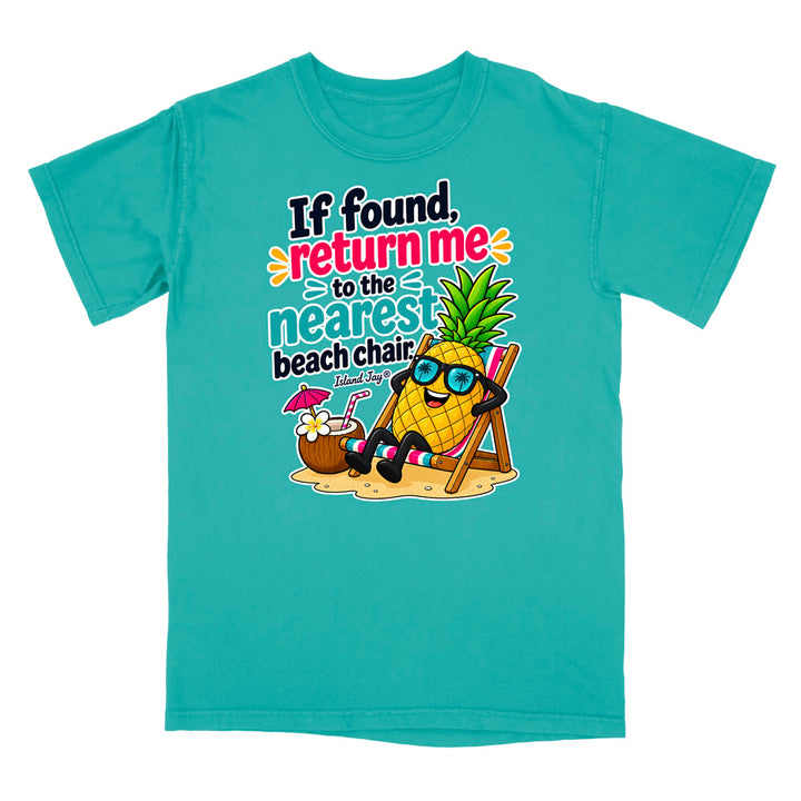 A turquoise short-sleeve crewneck t-shirt featuring a colorful graphic of a pineapple wearing sunglasses and relaxing in a beach chair next to a coconut drink, with the text 'If found, return me to the nearest beach chair' printed on the front.