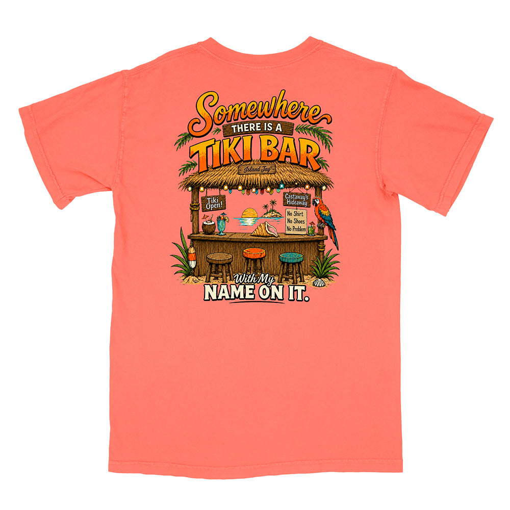 A coral pink short-sleeve t-shirt with a large graphic on the front depicting a tropical tiki bar scene with the text 'Somewhere THERE IS A TIKI BAR' and 'Your Name ON IT.'.