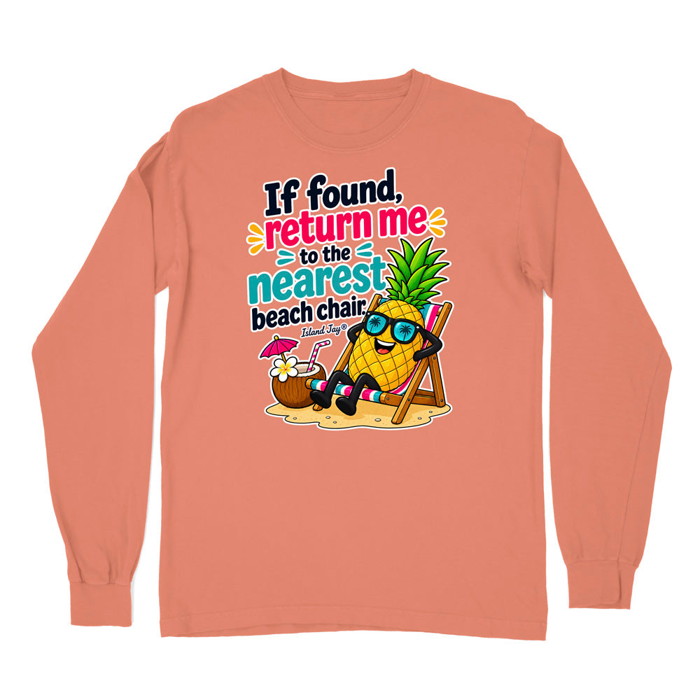 A peach-colored long-sleeve t-shirt with a colorful graphic on the front. The graphic features a cartoon pineapple wearing sunglasses and relaxing in a beach chair next to a coconut drink, with the text 'If found, return me to the nearest beach chair' and 'Tropical Pig'.