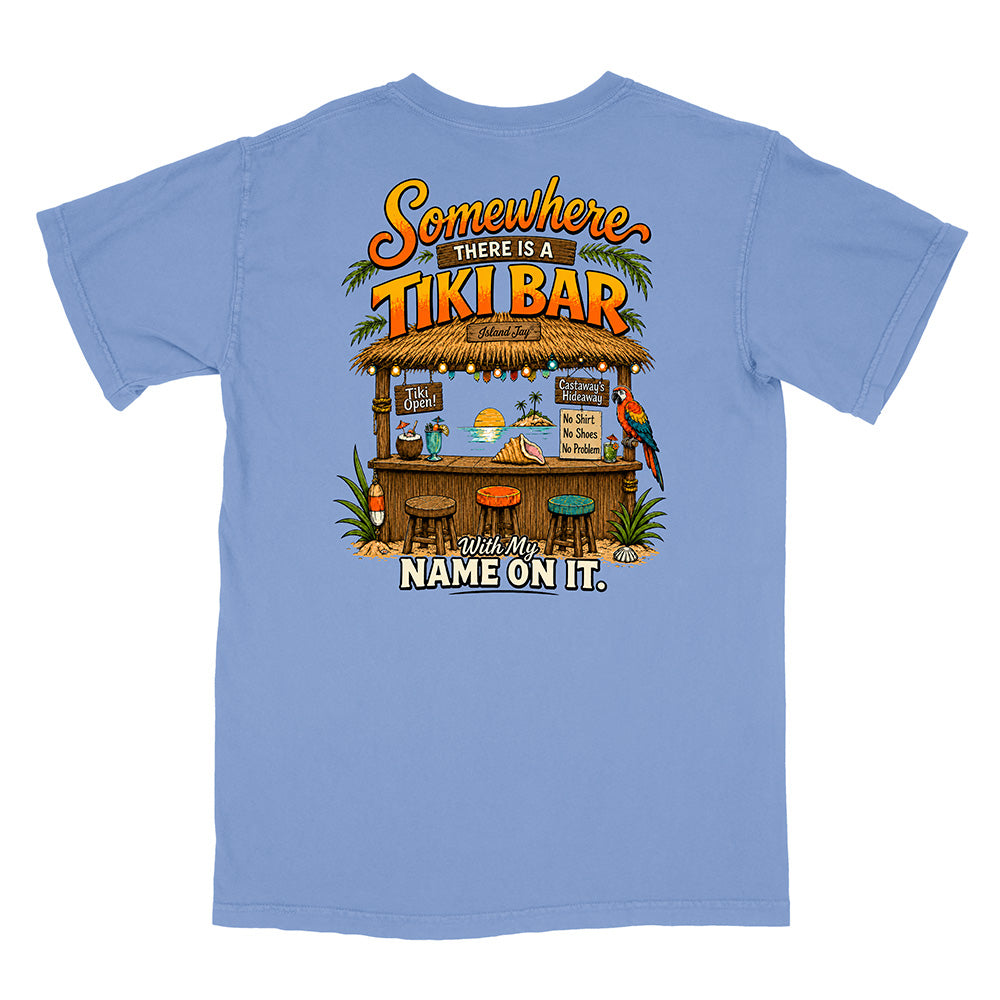 A light blue short-sleeve t-shirt shown flat against a white background, featuring a large graphic print on the back with a tropical tiki bar scene and the text 'Somewhere THERE IS A TIKI BAR With My NAME ON IT.'.