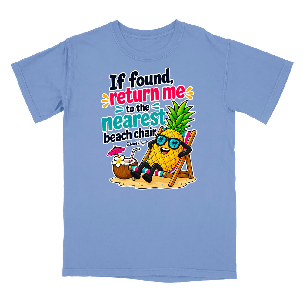 A light blue short-sleeve t-shirt with a colorful graphic on the front. The graphic features a cartoon pineapple wearing sunglasses and sitting in a beach chair next to a coconut drink, with the text 'If found, return me to the nearest beach chair' and 'Shark Ray'.