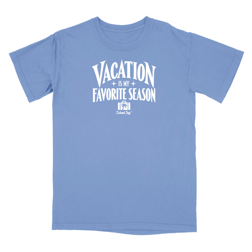 A light blue short-sleeve t-shirt with a white graphic print on the front that reads 'VACATION IS MY FAVORITE SEASON' with a small 'Kalamazoo Dog' logo underneath, displayed on a solid white background.